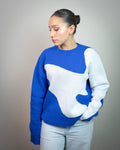 Mujer con suéter azul y blanco de diseño abstracto, jeans celestes, fondo neutro