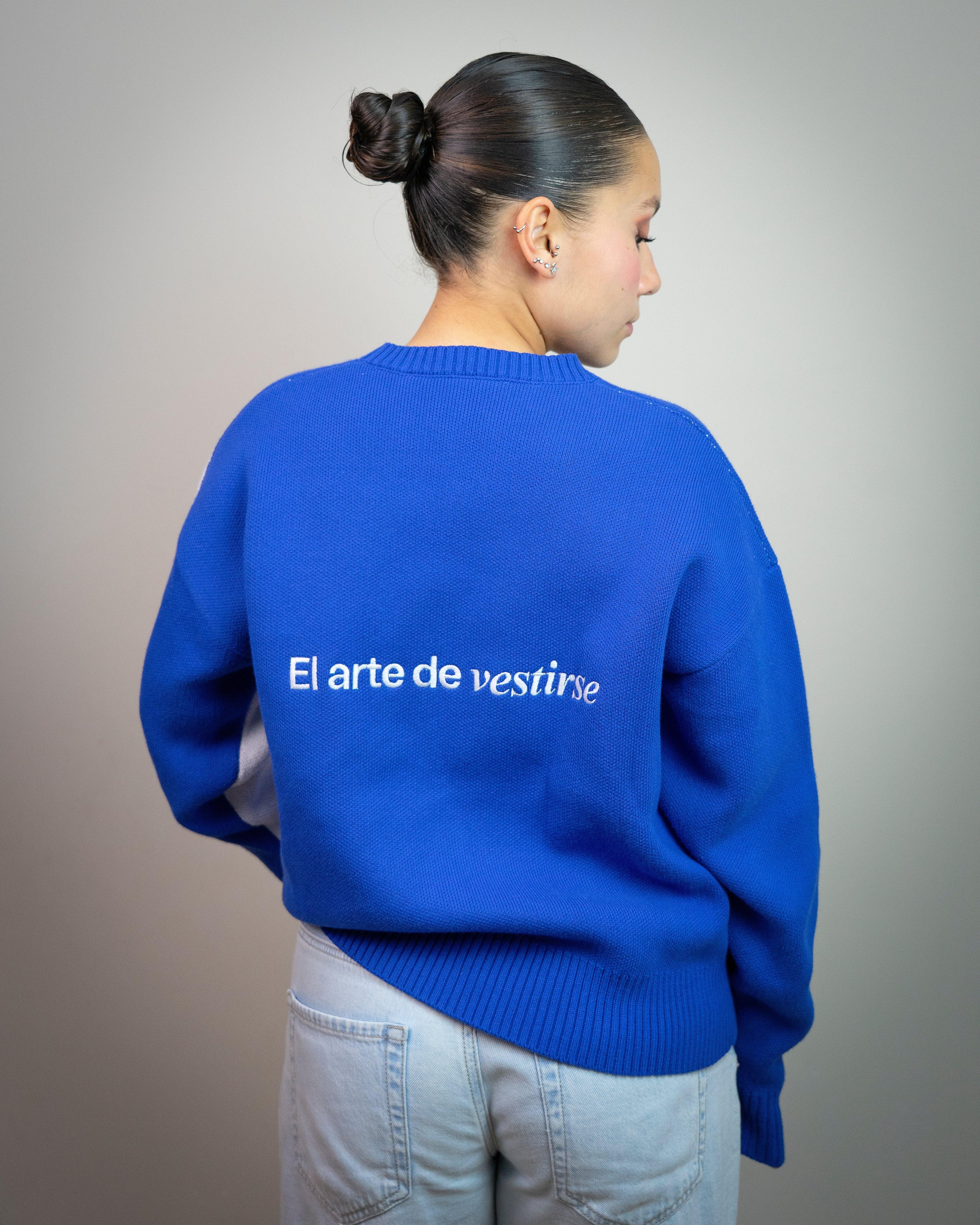 Mujer de espaldas con suéter azul que dice 'El arte de vestirse', moda casual moderna.