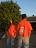 Pareja joven con camisetas oversize naranjas, estampado escorpión y letras, moda urbana